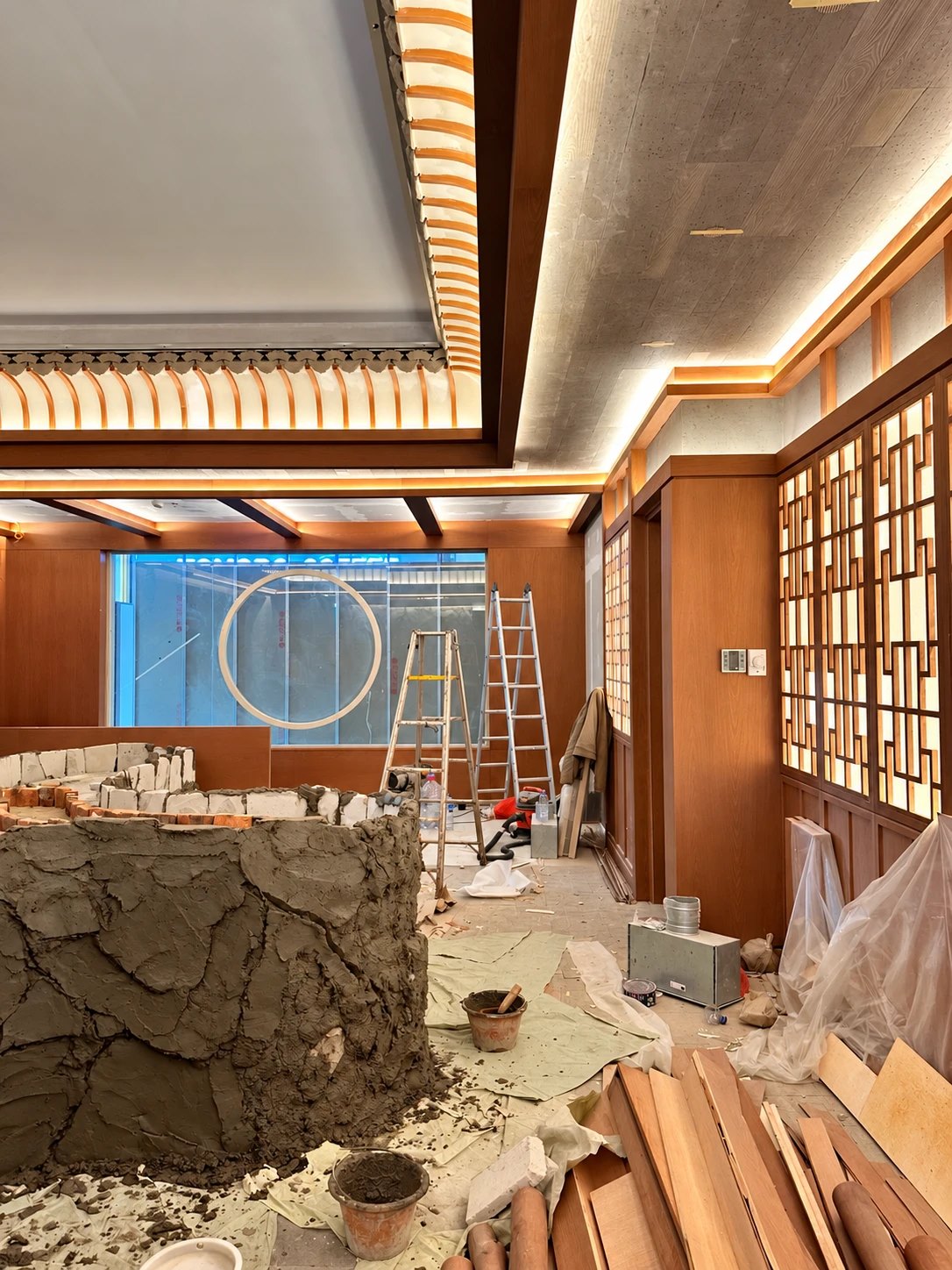 A restaurant interior under construction, with timber lattice screens and a rock garden being sculpted